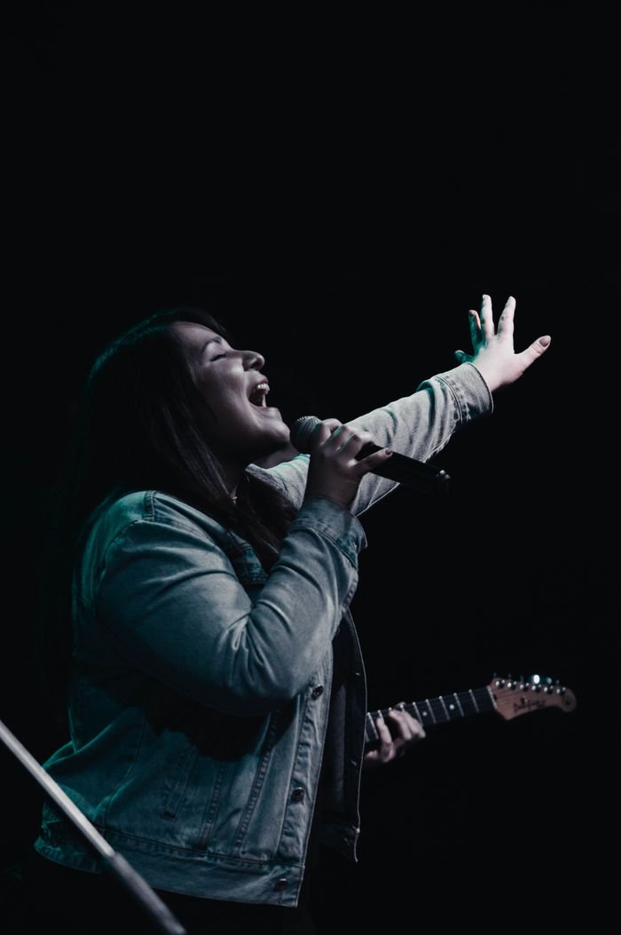 journey Woman singing passionately on stage in Mendoza, Argentina, holding a microphone.