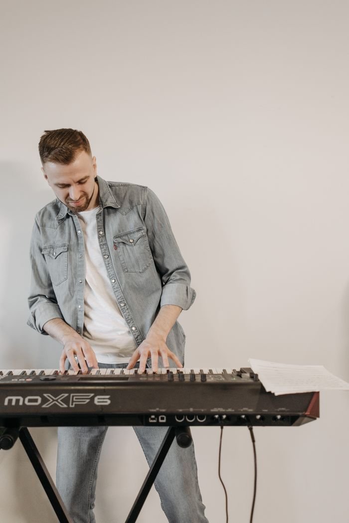 The Art of Drawing Readers In: Your attractive post title goes here A musician in a denim jacket plays a keyboard indoors with a focus on musical expression.